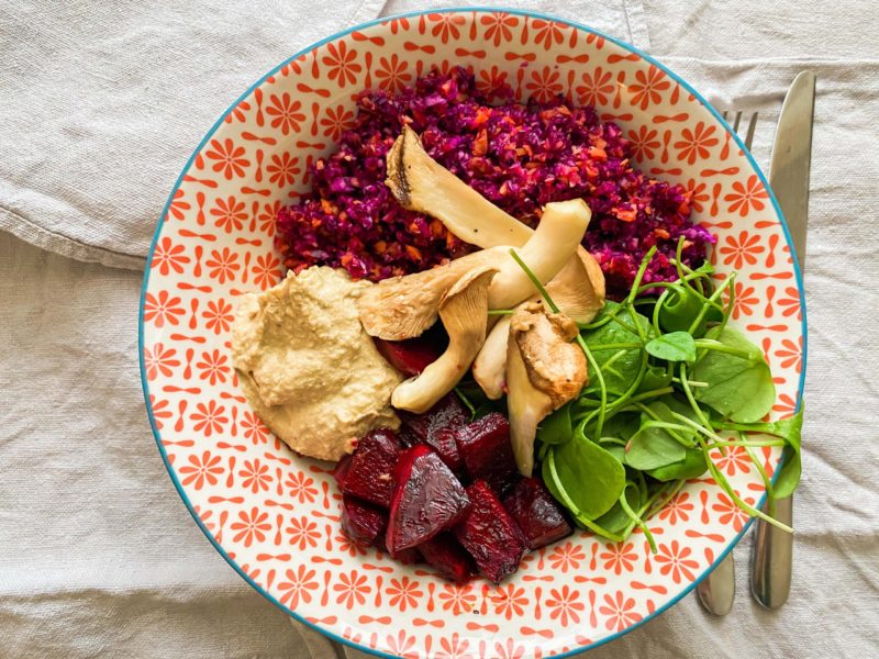 Pinke Buddha-Bowl mit Rotkohl-Karotten-Salat, gerösteter Rote Beete, gebratenen Pilzen und grünem Salat
