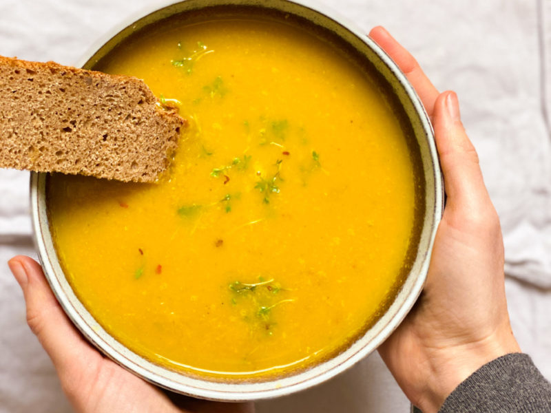 Gelbe Beete Suppe mit Linsen und Brot in Schüssel mit Händen
